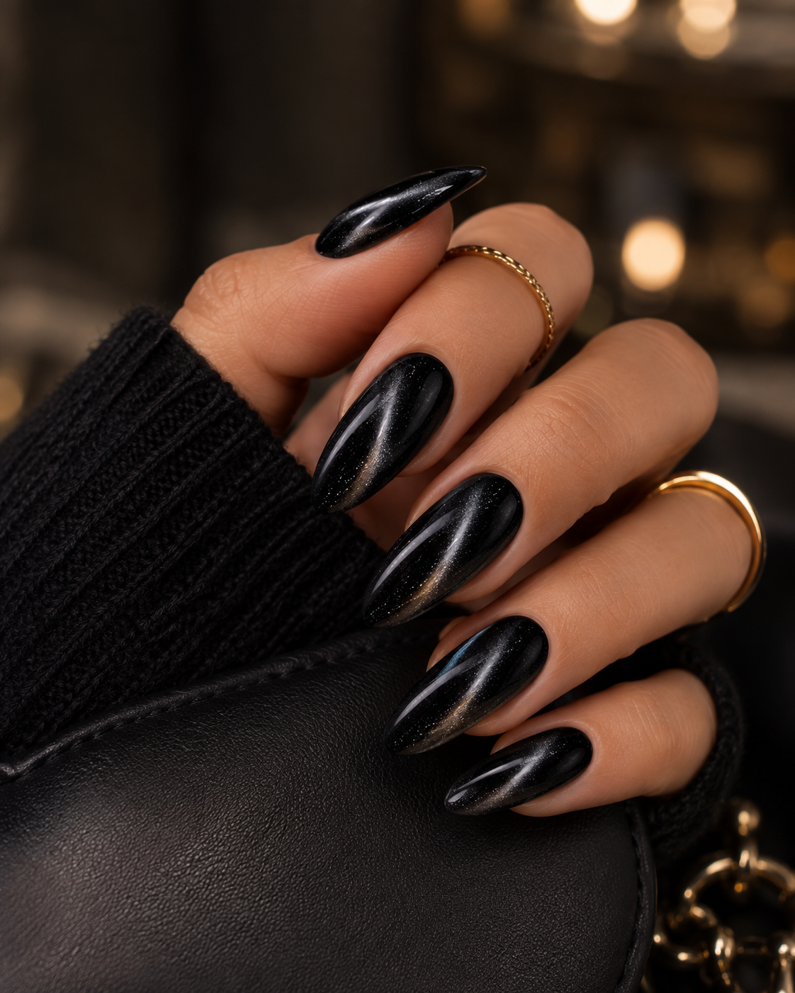 Jet black cat eye nails with a glossy magnetic shimmer on long almond-shaped nails holding a black leather clutch