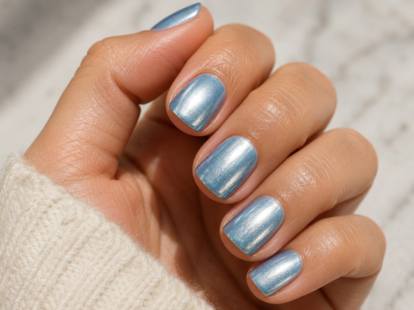 Close up of a frosted icy blue chrome manicure with a metallic shimmer finish on short square nails