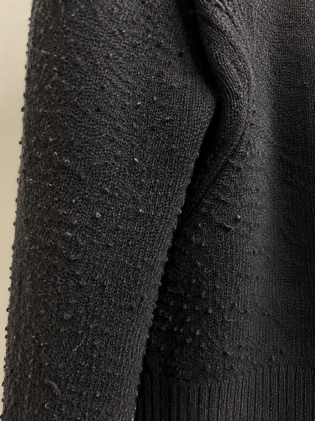 Close up of an acrylic knit sweater showing dense pilling across the sleeve and side seam