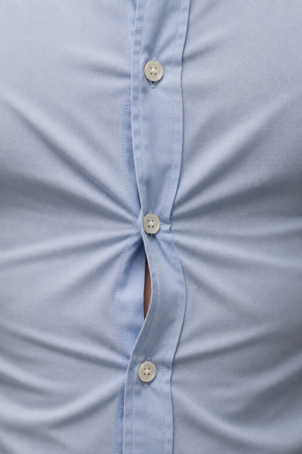 Close up of diagonal pull lines forming an X across a shirt button that is straining