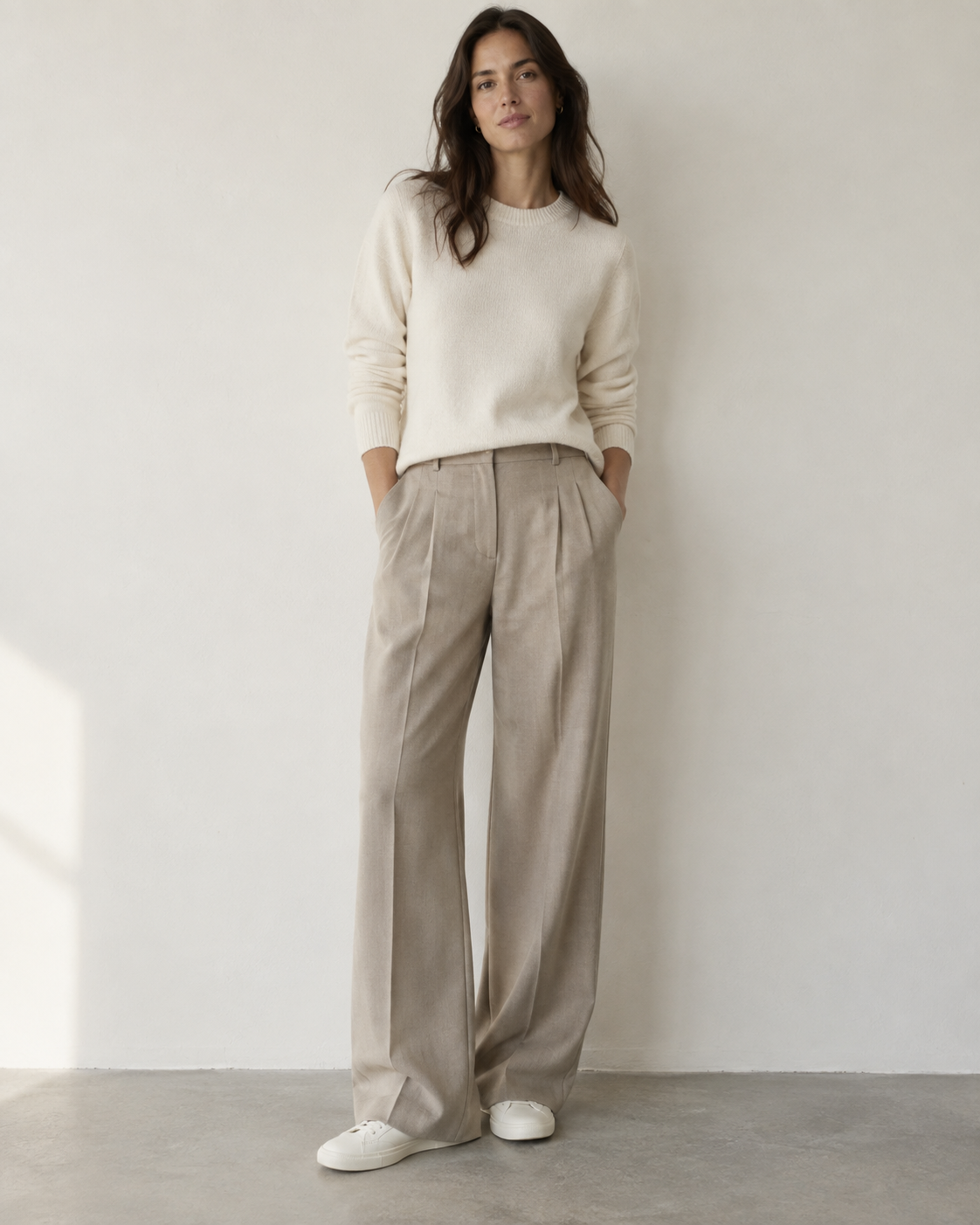 A woman wearing a simple cream sweater and tailored trousers that look relaxed but clearly well made